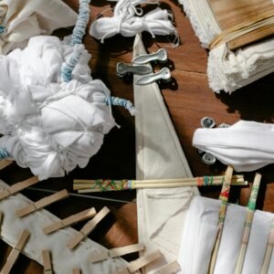 Overhead view of pleated fabrics tied with threads on table with pins and wooden block in sunlight